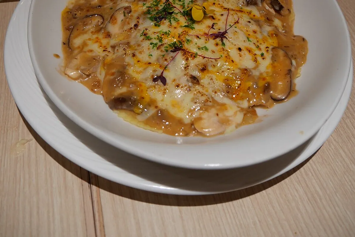 Baked ravioli with creamy mushroom sauce browned cheese and parsley