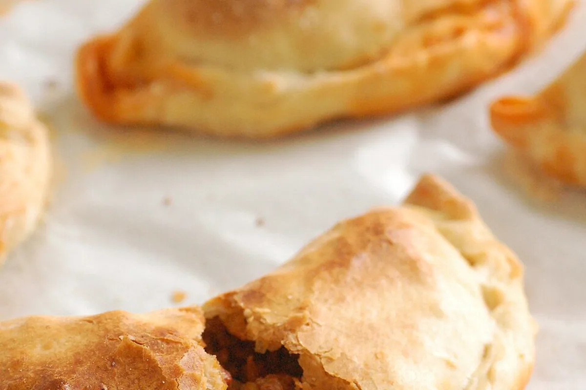 Golden baked beef empanadas with one opened to show the filling