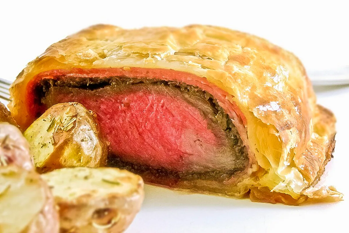 Beef Wellington cut open to show pink tenderloin mushroom duxelles and flaky pastry