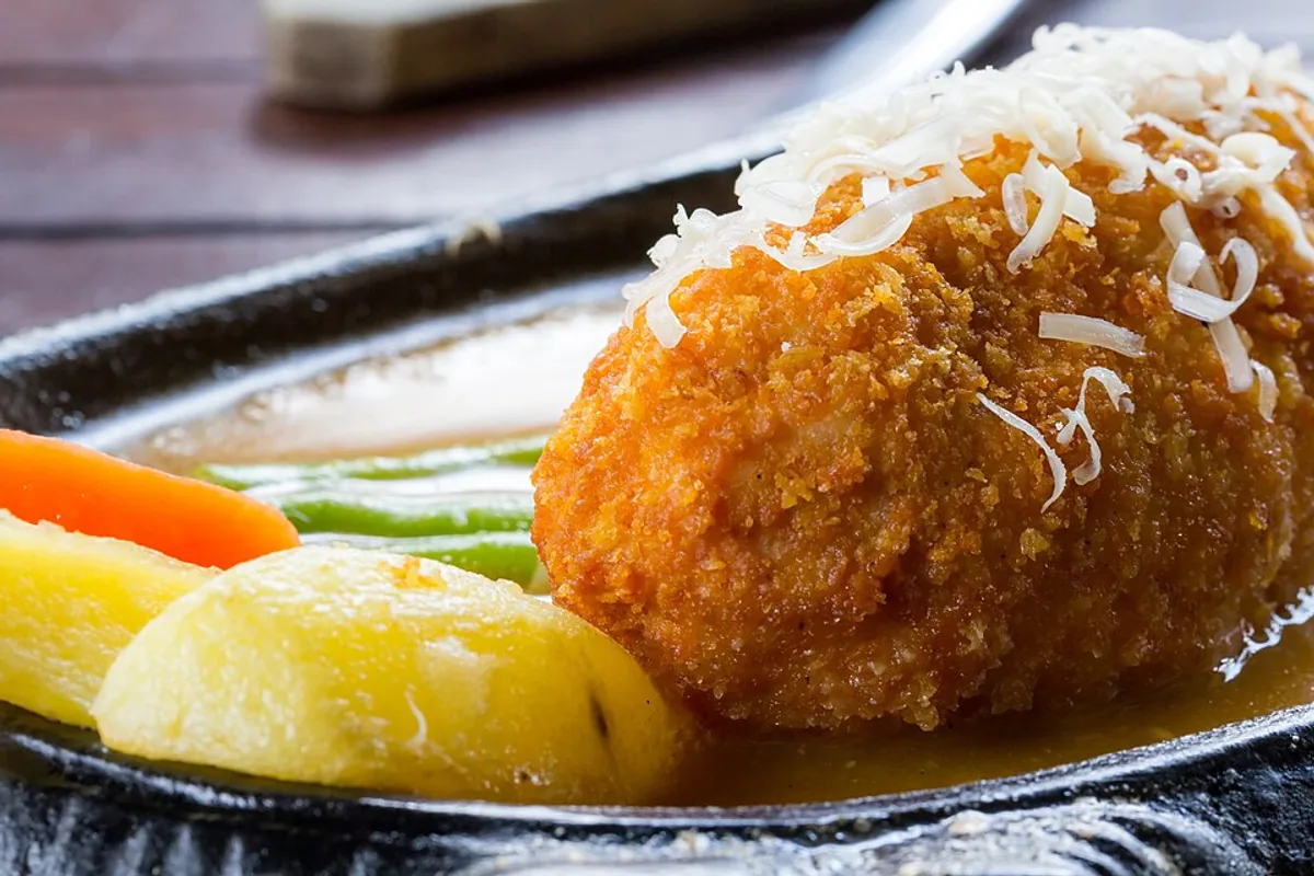 Crisp chicken cordon bleu cut open to show ham and melted cheese with potatoes and vegetables