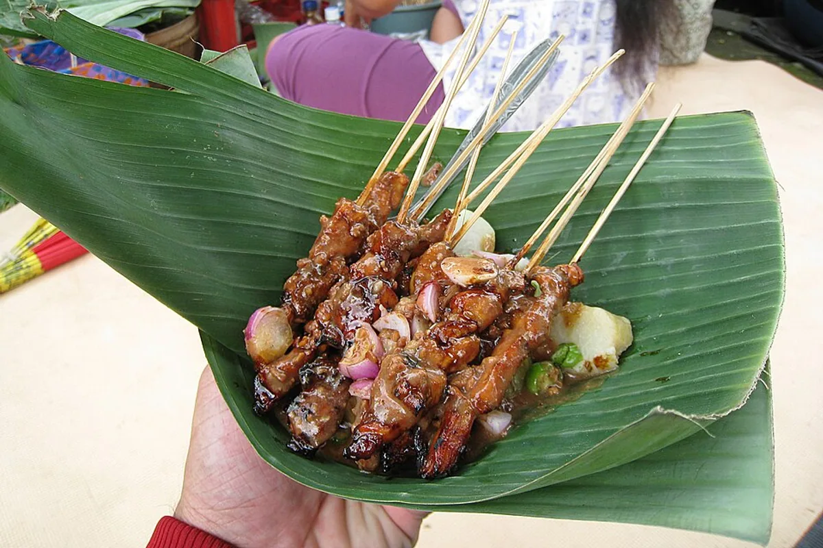 Grilled chicken satay skewers on a banana leaf with peanut sauce
