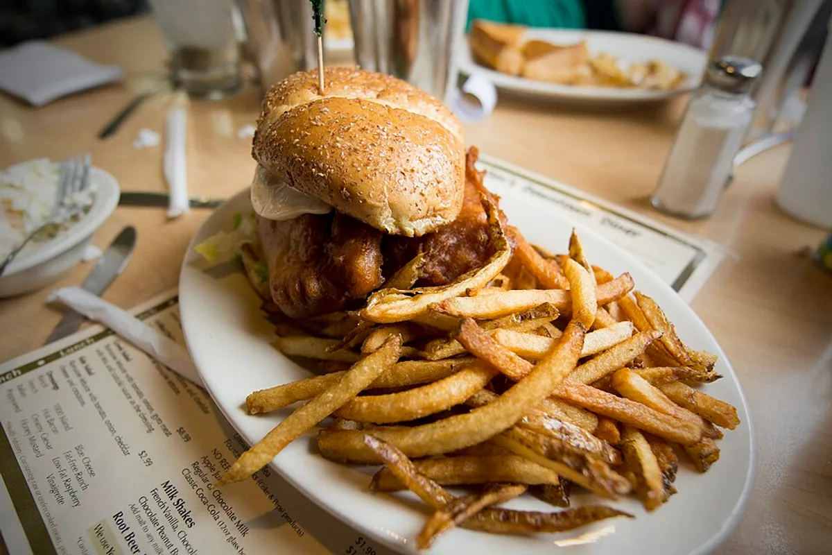 Crispy fish sandwich on a soft bun with a pile of curly fries