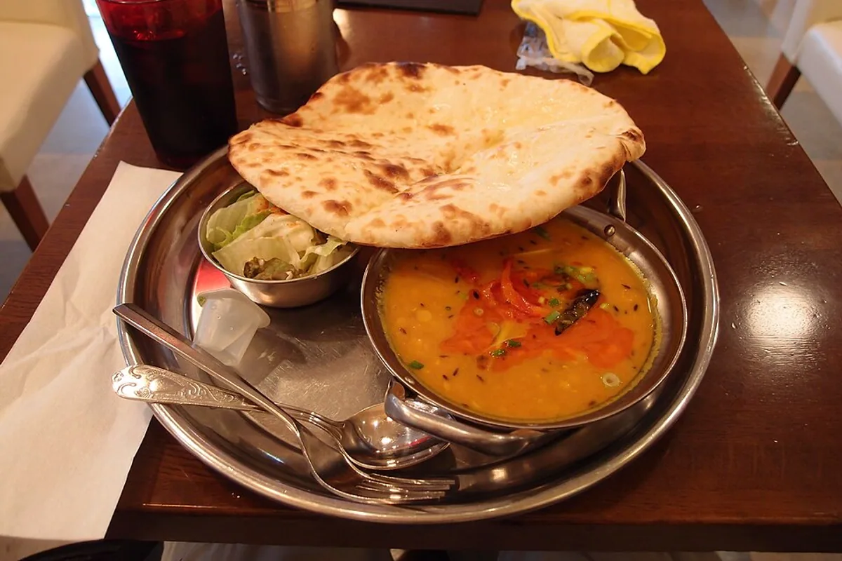 Bowl of red lentil dal curry with folded cheese naan