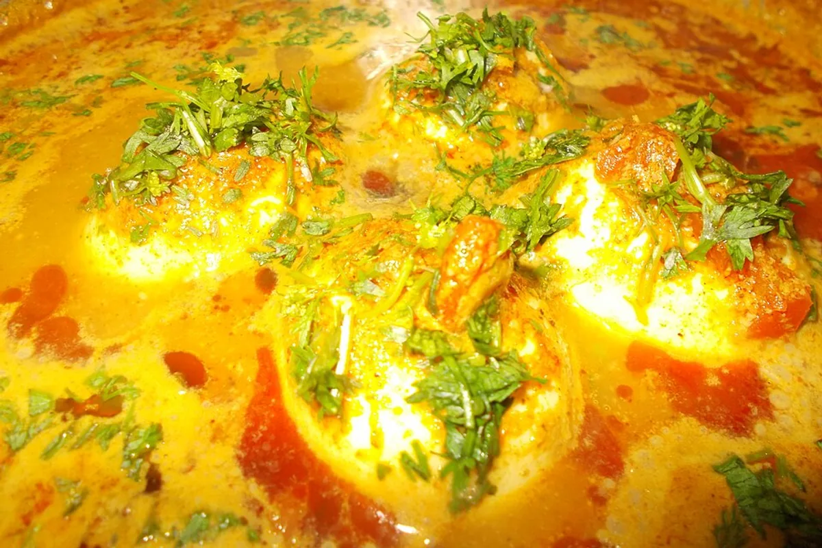 Halved boiled eggs in tomato curry with cilantro and rice
