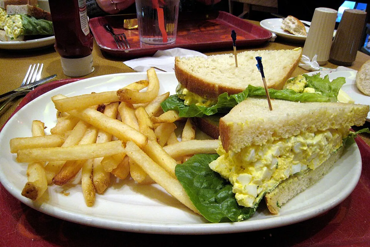 Egg salad sandwich served with fries and a green salad
