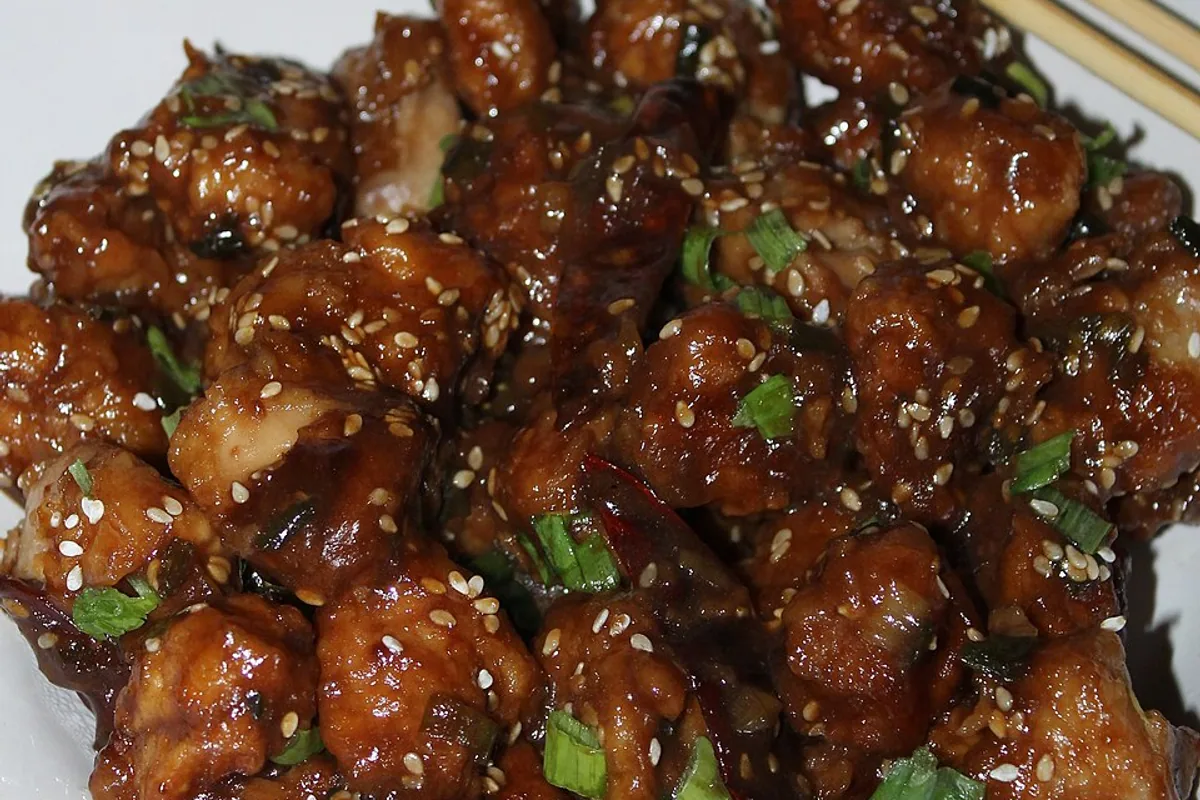 Glossy honey sesame chicken pieces with sesame seeds and scallions