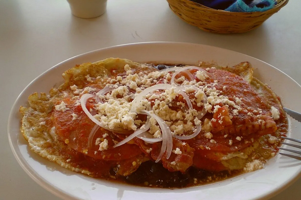 Huevos rancheros with fried eggs red salsa sliced onion and crumbled cheese