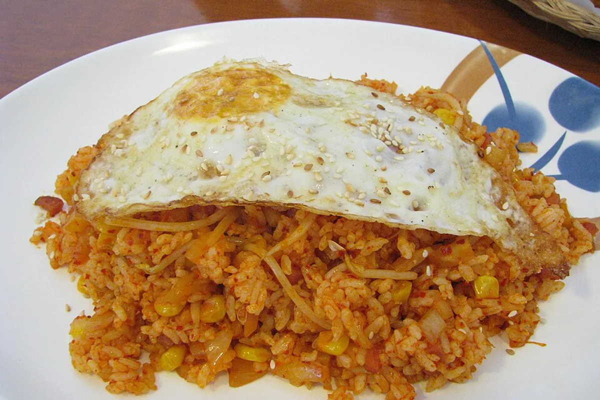 Red kimchi fried rice with corn topped with a fried egg and scallions