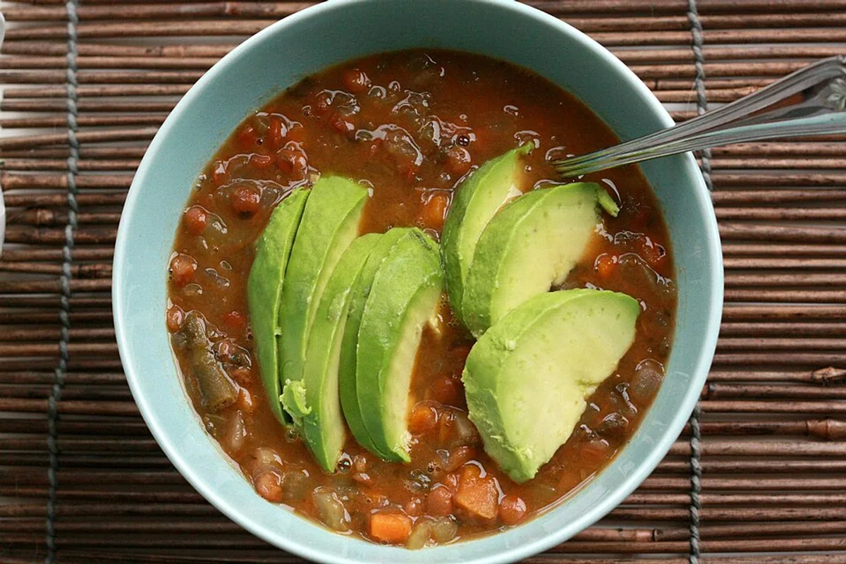 Lentil and vegetable soup topped with sliced avocado