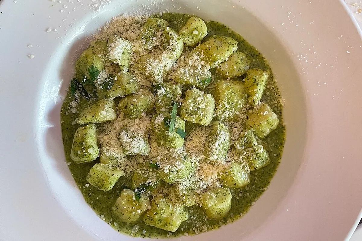Potato gnocchi coated in green basil pesto with herbs and grated Parmesan