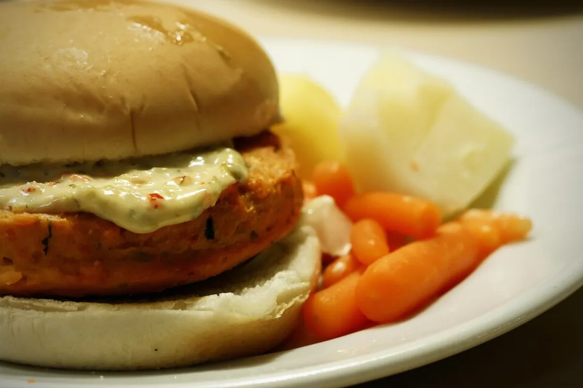 Fresh salmon burger on a bun with lettuce and creamy herb sauce