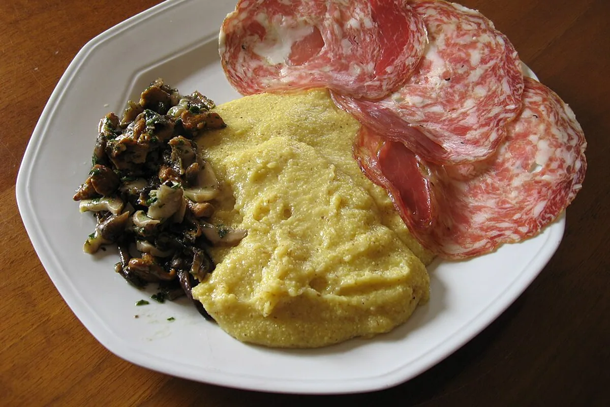 Creamy yellow polenta with sauteed mushrooms and sliced soppressa