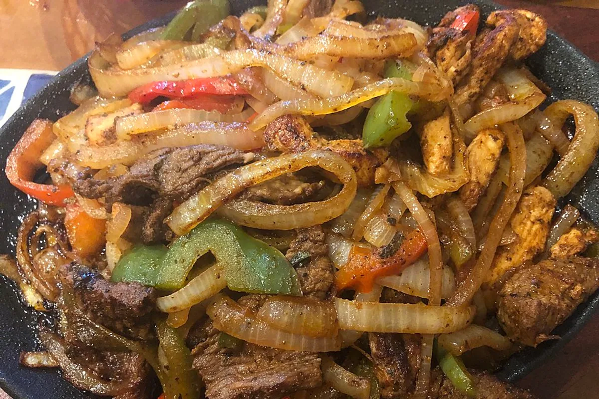 Sizzling chicken and steak fajitas with peppers and onions