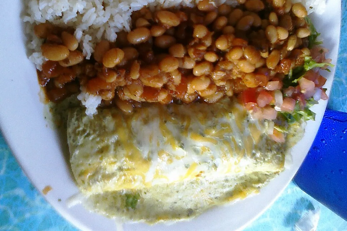 Grilled fish taco with cabbage and green sauce beside pinto beans and rice